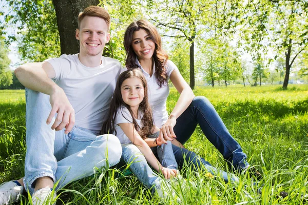 春の公園に座っている3人の家族牧草地草が幸せであること — ストック写真