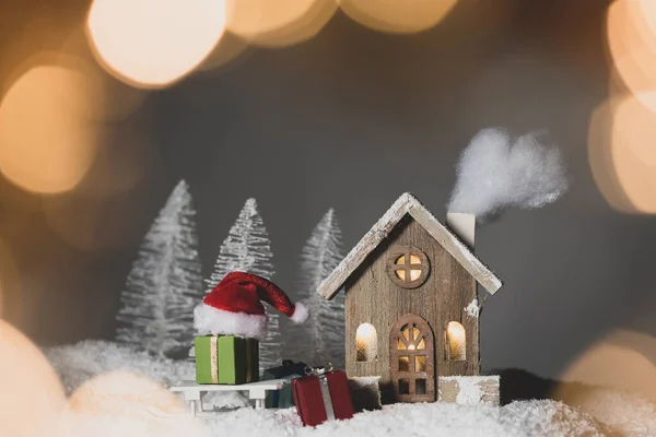 Рождественская Открытка Небольшим Светящимся Декоративным Домом Подарками Кепкой Санта Клауса — стоковое фото