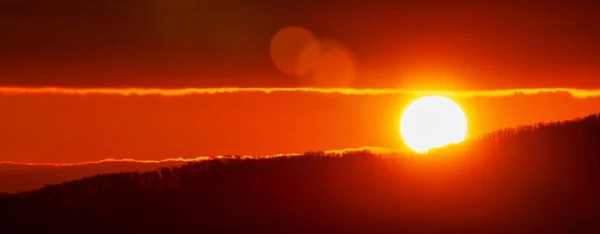 Amazing sunrise in mountains, sunny disk rises from tops of hill. Natural lens flare in sky, sunbeam light leaks