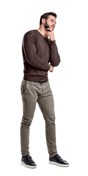 Een bebaarde man in smart casual kleding staat in volle hoogte met één hand op zijn kin aan te raken. — Stockfoto