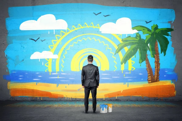 A businessman stands with his back turned and looking at a finished wall picture of exotic isle.