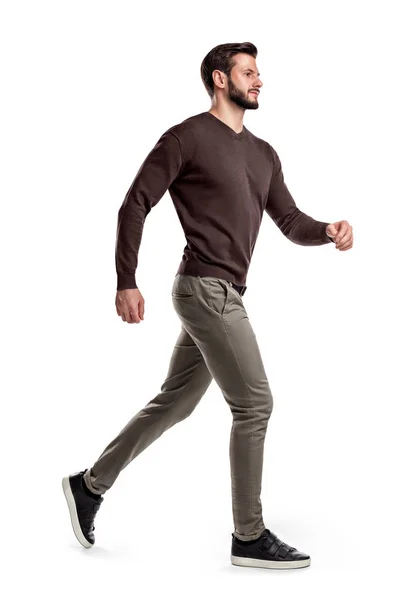Un giovane uomo barbuto in una vista laterale cammina veloce sul punto di correre su uno sfondo bianco . — Foto Stock