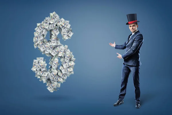 Ένας επιχειρηματίας φορώντας ένα καπέλο μάγοι και παρουσιάζει ένα μεγάλο σύμβολο δολαρίου κατασκευασμένα από πολλούς λογαριασμούς. — Φωτογραφία Αρχείου