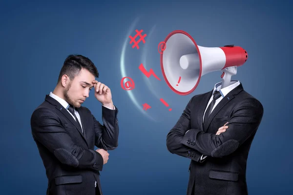 A troubled businessman stands near another man with a large shouting megaphone instead of his head. — Stock Photo, Image