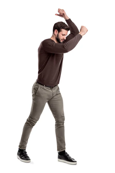 Un joven barbudo en forma con ropa casual intenta golpear o romper algo sosteniendo una herramienta invisible . — Foto de Stock