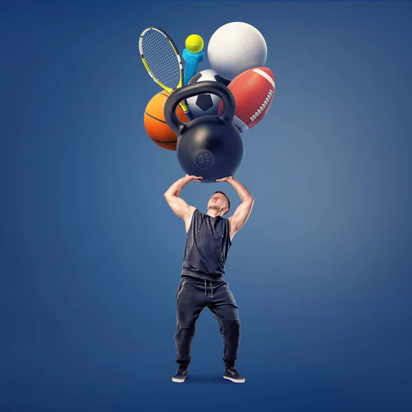Um atleta segura acima de sua cabeça um kettlebell pesado gigante, um dumbbell, uma raquete, e várias bolas para jogos diferentes . — Fotografia de Stock