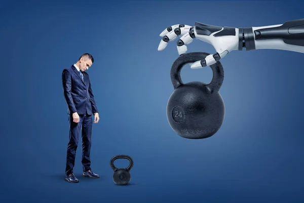 A sad businessman stands near a kettlebell with a robotic hand lifting and giving him another huge one weight.