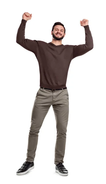 Un hombre barbudo feliz está de pie en ropa casual sonriendo y sosteniendo los brazos en la victoria en puños apretados . —  Fotos de Stock