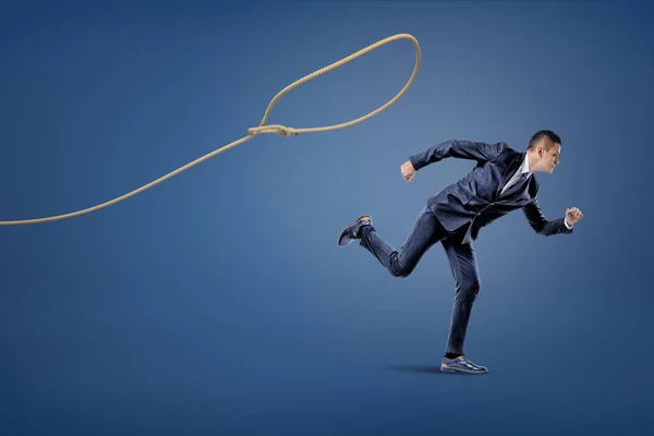Un hombre de negocios con traje huye de un lazo de cuerda que trata de atraparlo. . — Foto de Stock