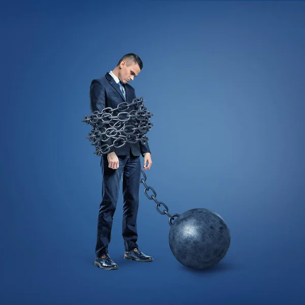 Een droevig teleurgesteld zakenman staat gebonden door een brede metalen ketting die is vergrendeld met een ijzeren bal. — Stockfoto