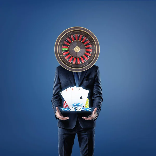 Un hombre de negocios con una ruleta de casino en lugar de su cabeza se para y ofrece cartas, dados y fichas de casino . — Foto de Stock