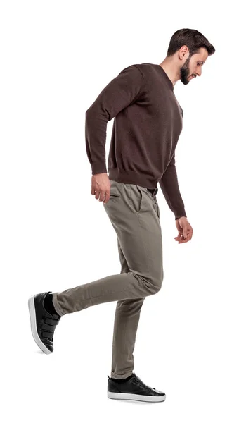 Um homem de aparência séria em roupas casuais caminha em uma visão lateral com uma perna dobrada atrás dele . — Fotografia de Stock