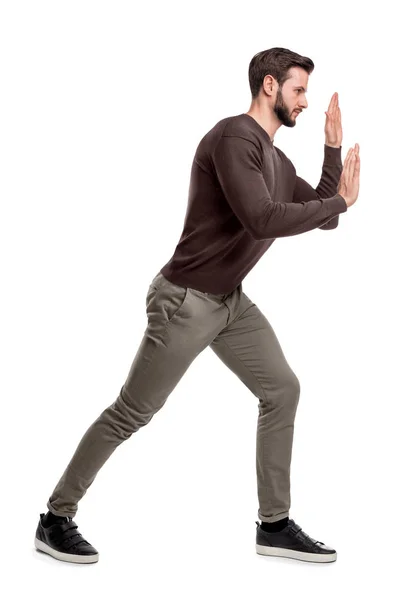 Un hombre barbudo en pantalones casuales presiona sus manos sobre un objeto invisible para moverlo . —  Fotos de Stock