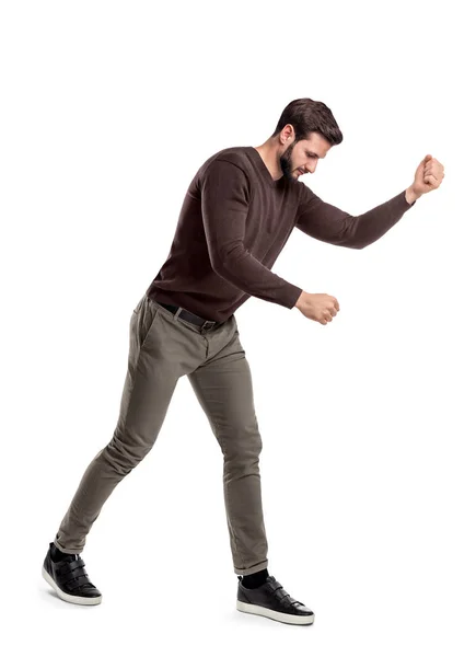 A fit bearded young man in casual clothes tries to hit or make something as if holding an invisible tool. — Stock Photo, Image