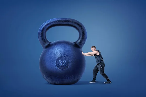 A muscular athlete ties to push and move from its place a huge iron kettlebell. — Stock Photo, Image