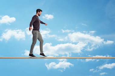 A casually dressed man with a beard walks carefully on a tight rope on a sky background. clipart
