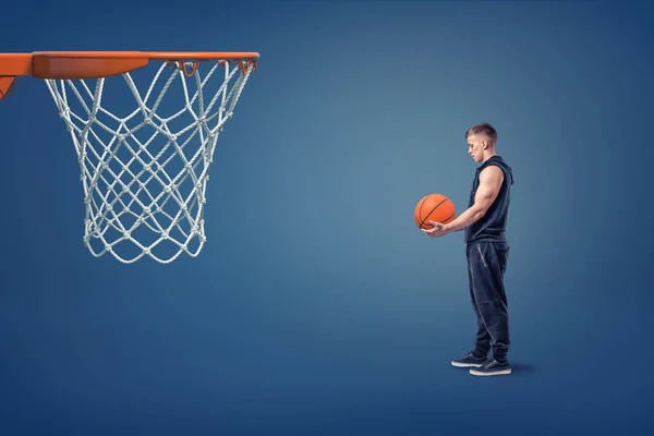 Un joven atleta con una pelota de baloncesto en sus manos se para cerca de un aro naranja . — Foto de Stock