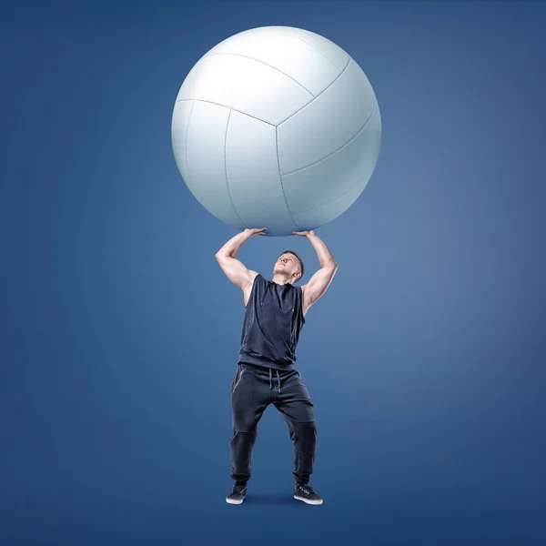 Un pequeño atleta muscular sostiene una gran bola de voleibol blanco en brazos rectos por encima de sí mismo . —  Fotos de Stock