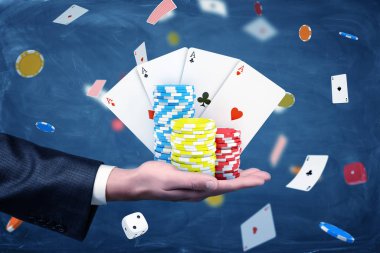 Casino fişi ve iskambil kartları ve zar dolu bir arka plan ile tutan bir businessmans el.