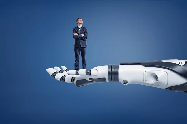 Un piccolo imprenditore pensante alza lo sguardo in piedi su un enorme braccio robotico . — Foto Stock