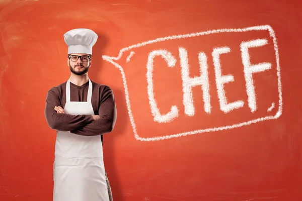 Hombre con delantal de cocina y sombrero de chef con un cartel sobre fondo rojo —  Fotos de Stock