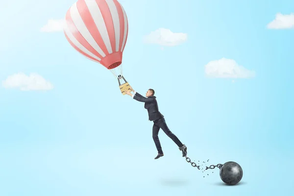 Бизнесмен отрывается от цепи и железного шара, чтобы поймать небольшой воздушный шар . — стоковое фото