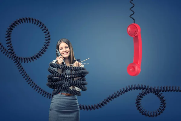 Uma empresária capturada e amarrada por grandes cabos de telefone preto perto de um receptor de telefone vermelho gigante . — Fotografia de Stock