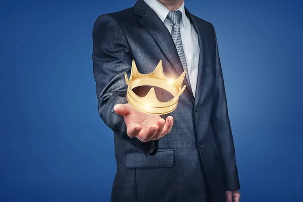 Een heldere gouden kroon hangt recht boven de hand van een businessmans en sparkles. — Stockfoto