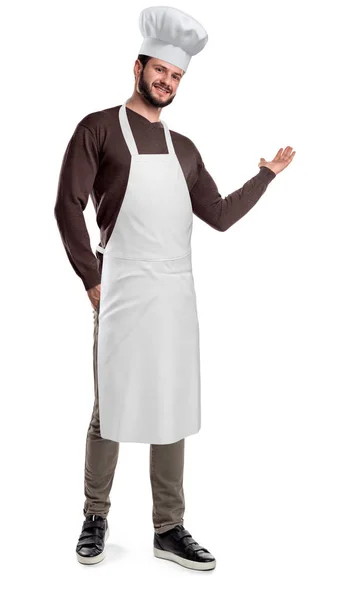 A bearded cook wears an apron and hat and makes an inviting gesture on a white background. — Stock Photo, Image