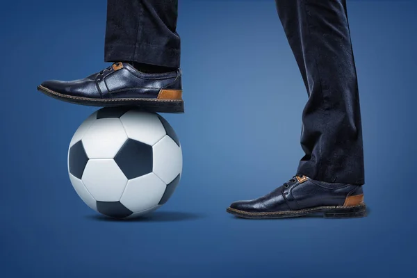 Gigantes hombres de negocios piernas con un pie de pie en una pelota de fútbol sosteniéndolo en su lugar . —  Fotos de Stock