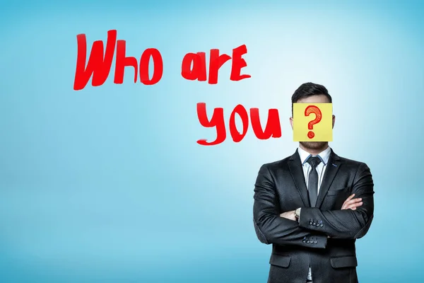 Ένας επιχειρηματίας με έξυπνο κοστούμι, πρόσωπο κρυμμένο πίσω από ένα κίτρινο αυτοκόλλητο σημείωμα με ένα ερωτηματικό σχετικά με το που τελειώνει το ποιος είναι ερώτηση σας. — Φωτογραφία Αρχείου