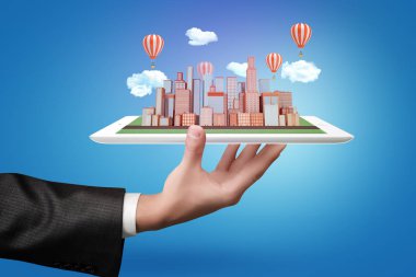 Bir tablet şehir gökdelenler ile mavi arka plan üzerinde modeli, bulutlar ve hava balonları tutan işadamı el