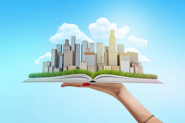 Vrouwelijke hand met wolkenkrabbers van de stad op een open boek op blauwe achtergrond — Stockfoto