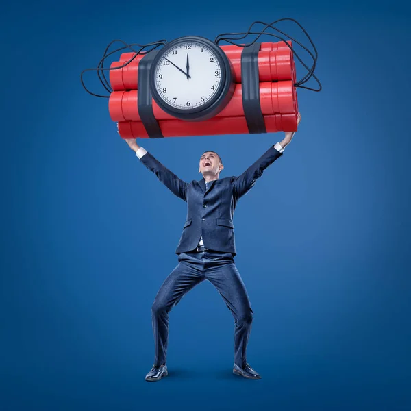 A joyful businessman in smart suit holding up a huge bundle of dynamite with a time bomb attached to it. — Stock Photo, Image