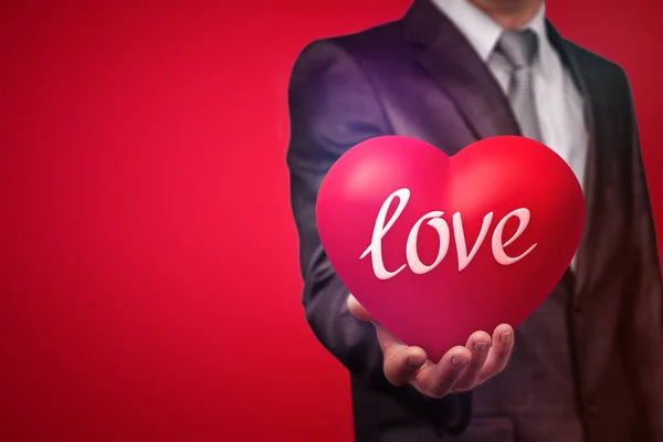 Imagen de la cosecha del hombre en traje sosteniendo un gran corazón rojo con la palabra amor sobre fondo rojo . — Foto de Stock