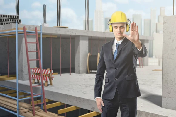 Üzletember, sárga bukósisak viselése, és bemutatja a stop gesztus építkezésen — Stock Fotó