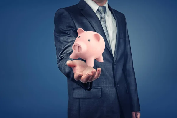 Een zakenman met verborgen gezicht toont een hand met een roze spaarvarken zweven boven het. — Stockfoto