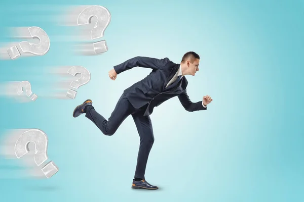 Businessman running from grey question marks on blue background