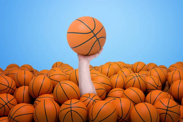 Ręka pojawiające się spośród sterty pomarańczowy koszykówki piłki gospodarstwa jeden na niebieskim tle — Zdjęcie stockowe