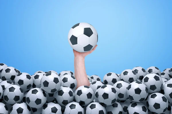 Mans mão emergindo de baixo de um monte de bolas de futebol e segurando um futebol para cima . — Fotografia de Stock