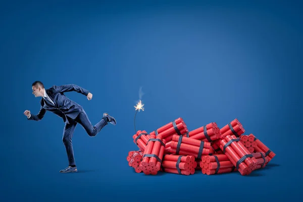 Zakenman weglopen pack van rode tnt dynamiet stokken met verlichte zekering op blauwe achtergrond — Stockfoto