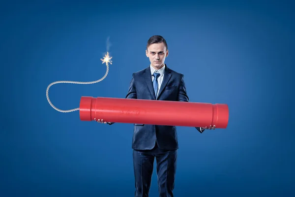 Jonge zakenman houden grote rode tnt dynamiet stok met verlichte zekering op blauwe achtergrond — Stockfoto
