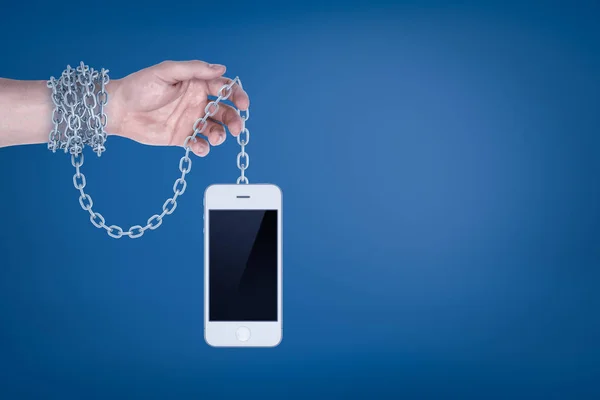 Male hand chained to white smart phone on blue background