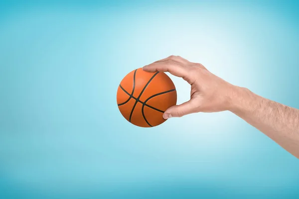 Acercamiento lateral de la mano del hombre sosteniendo poco baloncesto sobre fondo azul claro . — Foto de Stock