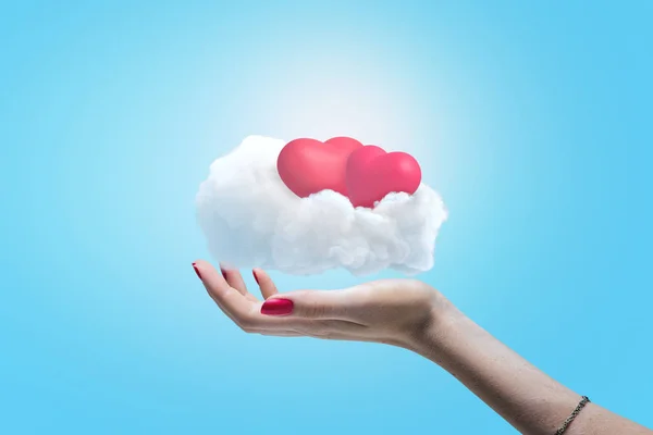 Γυναικείο χέρι που κρατά το λευκό σύννεφο με δύο ροζ καρδιές σε φόντο μπλε του ουρανού — Φωτογραφία Αρχείου