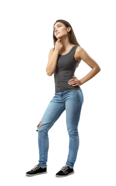 Junge Frau in ärmellosem Oberteil und blauer Jeans, die in halber Drehung steht, die linke Hand auf der Hüfte und der rechte Arm reiben sich unter dem Kinn isoliert auf weißem Hintergrund. — Stockfoto