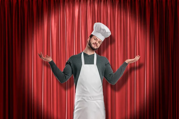 Küchenchef mit Kochschürze und Kochmütze hält Hände hoch auf rotem Bühnenvorhang — Stockfoto