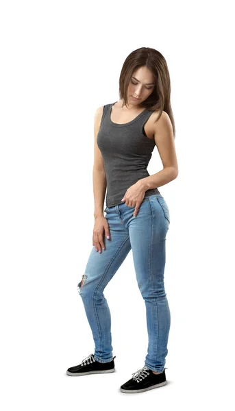 Junge Frau in ärmellosem Top und Jeans, die in halber Drehung steht und isoliert auf weißem Hintergrund nach unten schaut. — Stockfoto