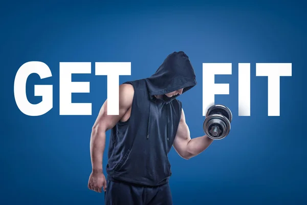 Athletic man in sleeveless hoody posing half-turn with dumbell in one hand on blue background with title GET FIT. — Stock Photo, Image