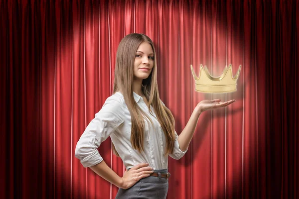 Young business woman holding golden crown on red stage curtains background